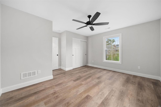 unfurnished bedroom with a closet, wood finished floors, visible vents, and baseboards