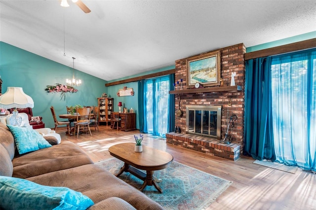 living room featuring brick wall, ceiling fan with notable chandelier, hardwood / wood-style floors, a fireplace, and lofted ceiling