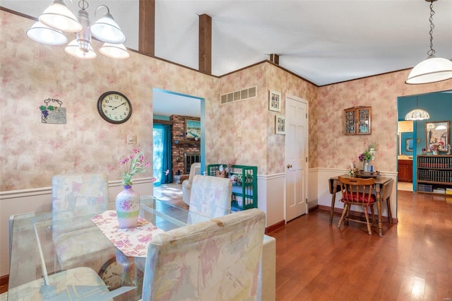 dining area featuring brick wall, a brick fireplace, hardwood / wood-style floors, vaulted ceiling, and an inviting chandelier