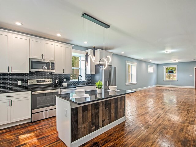 kitchen featuring appliances with stainless steel finishes, hanging light fixtures, a kitchen island, white cabinetry, and dark wood-type flooring