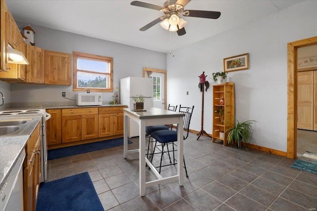 kitchen featuring baseboards, a kitchen bar, white appliances, a ceiling fan, and dark tile patterned flooring