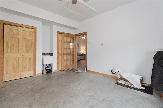 interior space featuring ceiling fan, attic access, concrete floors, and baseboards
