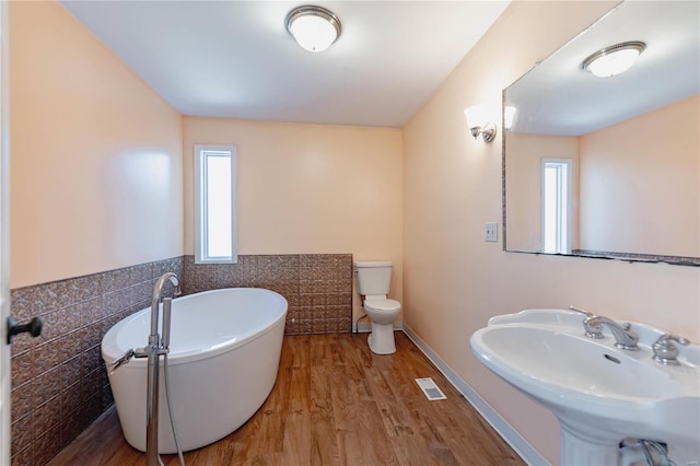 bathroom with wood-type flooring, sink, tile walls, toilet, and a bathing tub