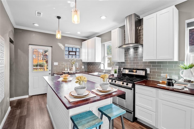 kitchen featuring wall chimney exhaust hood, dark wood-type flooring, hanging light fixtures, stainless steel gas range, and sink