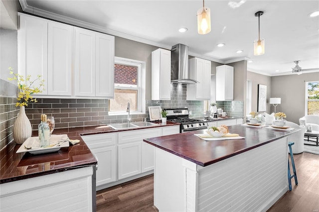 kitchen featuring wall chimney range hood, gas range, sink, decorative light fixtures, and plenty of natural light