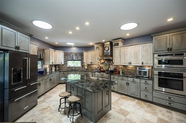 kitchen featuring light tile patterned floors, dark stone counters, a center island, wall chimney exhaust hood, and high end appliances