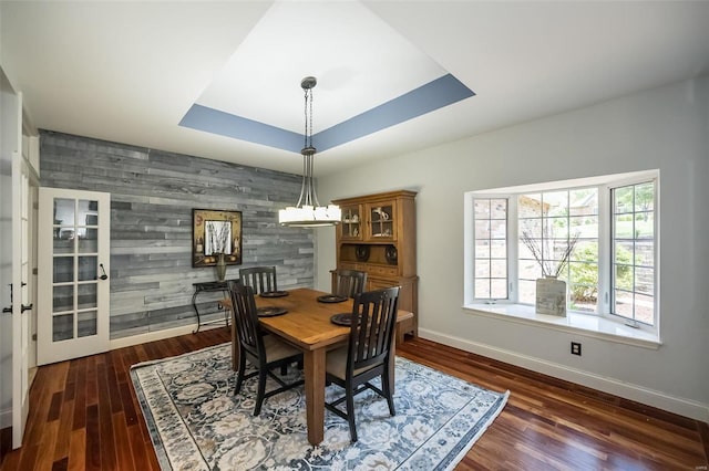 dining space with dark hardwood / wood-style flooring, wooden walls, and a tray ceiling