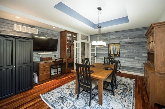 dining space with a tray ceiling, wood walls, and dark hardwood / wood-style flooring