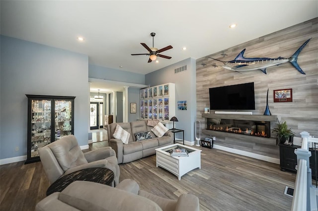 living room with wooden walls, dark wood-type flooring, and ceiling fan