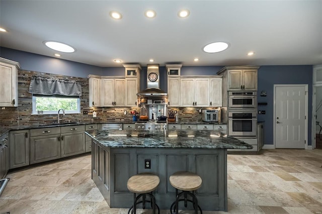 kitchen with dark stone countertops, a center island, double oven, wall chimney exhaust hood, and sink