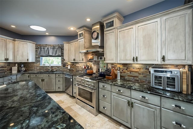 kitchen with wall chimney exhaust hood, dark stone countertops, appliances with stainless steel finishes, light tile patterned floors, and backsplash