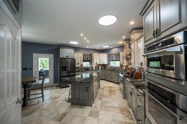 kitchen featuring tasteful backsplash, dark stone counters, a kitchen island, stainless steel appliances, and a kitchen bar