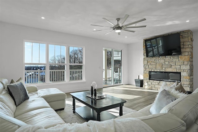 living room with ceiling fan, a fireplace, a water view, and light hardwood / wood-style flooring