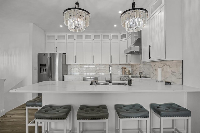 kitchen featuring stainless steel appliances, sink, wall chimney range hood, a notable chandelier, and hanging light fixtures