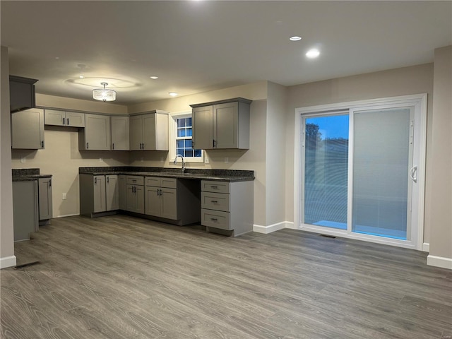 kitchen with dark stone countertops, hardwood / wood-style flooring, sink, and gray cabinetry