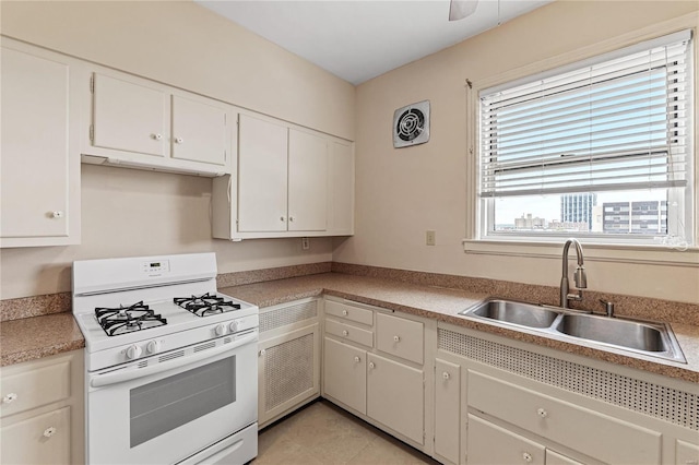 kitchen featuring sink, white cabinetry, light tile patterned floors, ceiling fan, and white gas range oven