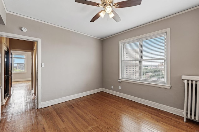 spare room with hardwood / wood-style floors, crown molding, radiator heating unit, and ceiling fan