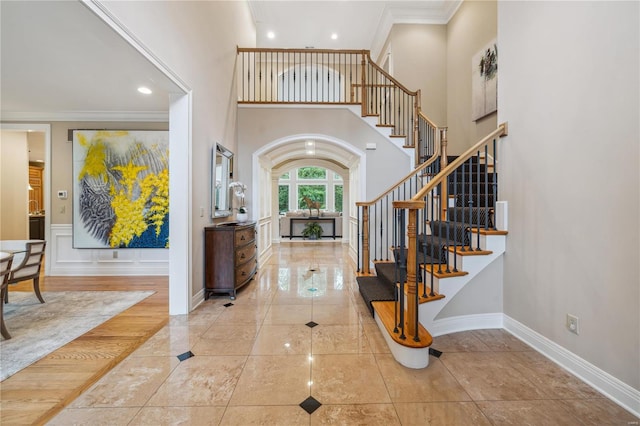 foyer entrance with light hardwood / wood-style floors, a towering ceiling, and ornamental molding