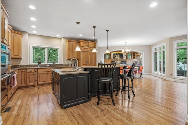 kitchen with light stone counters, an island with sink, hanging light fixtures, and plenty of natural light