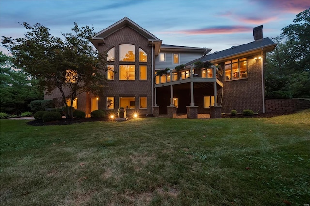 back house at dusk featuring central AC unit, a balcony, and a lawn