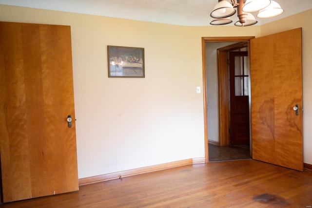 spare room featuring wood-type flooring and a chandelier