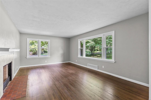 unfurnished living room featuring plenty of natural light, a tiled fireplace, and dark hardwood / wood-style flooring