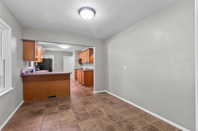 kitchen featuring kitchen peninsula, dark tile patterned floors, and black fridge