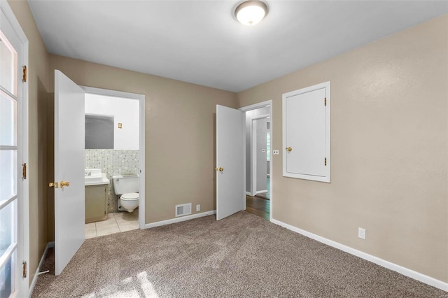 unfurnished bedroom featuring light carpet, ensuite bath, and tile walls