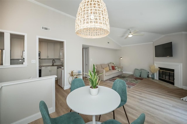 dining room featuring lofted ceiling, sink, crown molding, light wood-type flooring, and ceiling fan