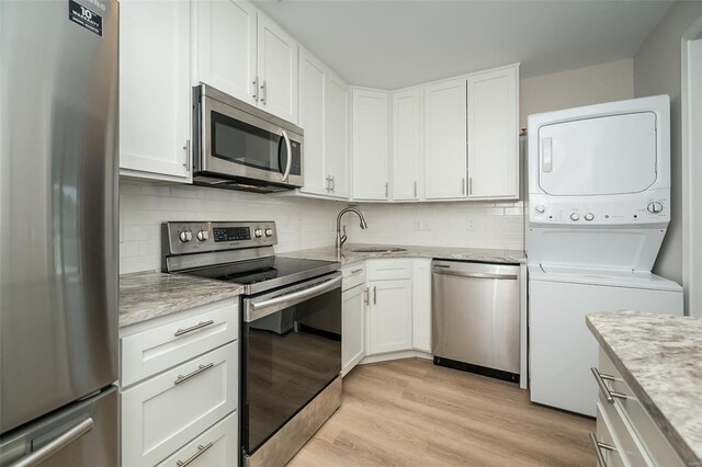 kitchen featuring white cabinetry, stainless steel appliances, light hardwood / wood-style flooring, and stacked washer and clothes dryer