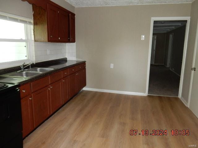 kitchen with stove, sink, light wood-type flooring, and decorative backsplash