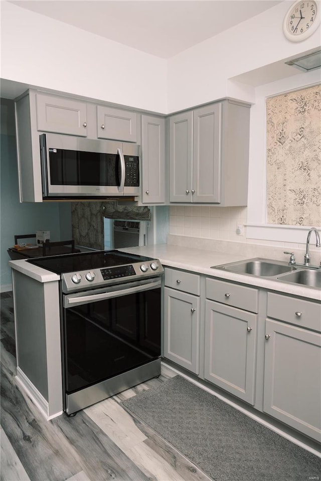 kitchen featuring sink, backsplash, gray cabinets, stainless steel appliances, and light hardwood / wood-style floors