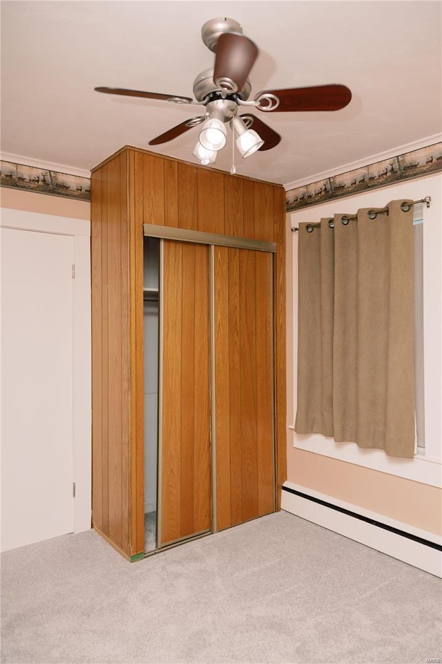 unfurnished bedroom featuring wooden walls, ceiling fan, a closet, light carpet, and baseboard heating