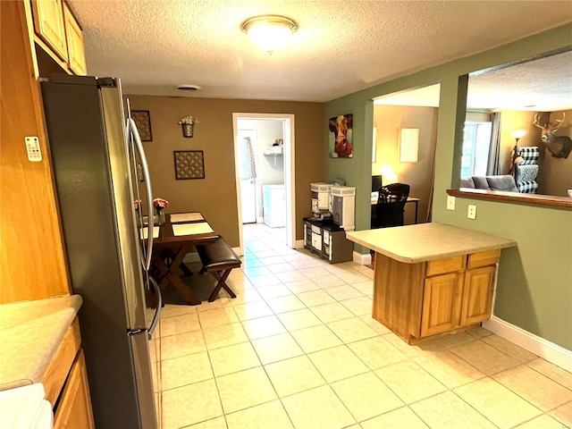 kitchen featuring independent washer and dryer, light tile patterned floors, stainless steel refrigerator, and kitchen peninsula