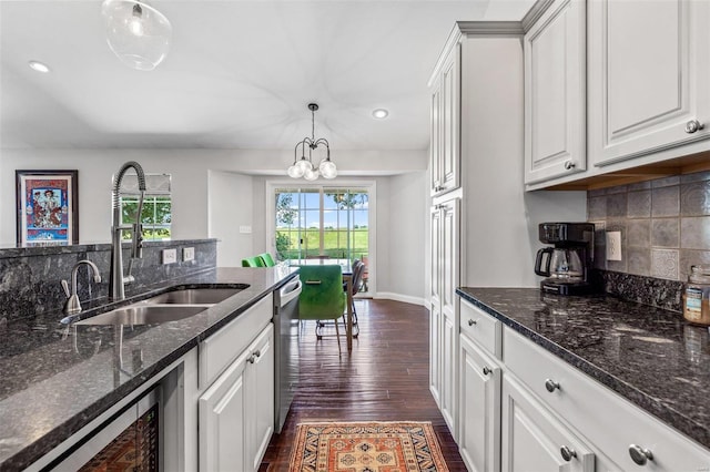 kitchen featuring dark stone countertops, pendant lighting, stainless steel dishwasher, white cabinets, and sink