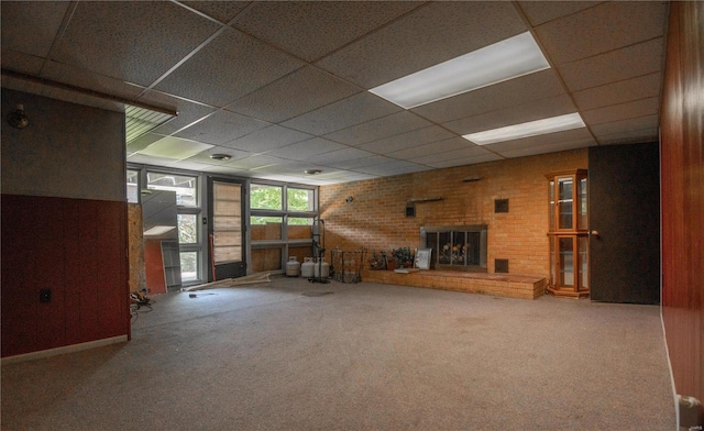 interior space featuring a fireplace, carpet, brick wall, and a paneled ceiling