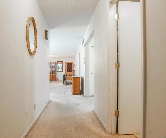 hallway with a textured ceiling and light colored carpet