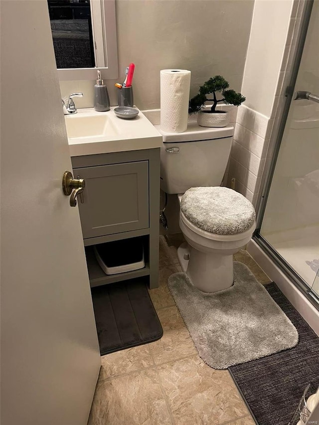 bathroom with a shower with shower door, vanity, tile patterned flooring, and toilet