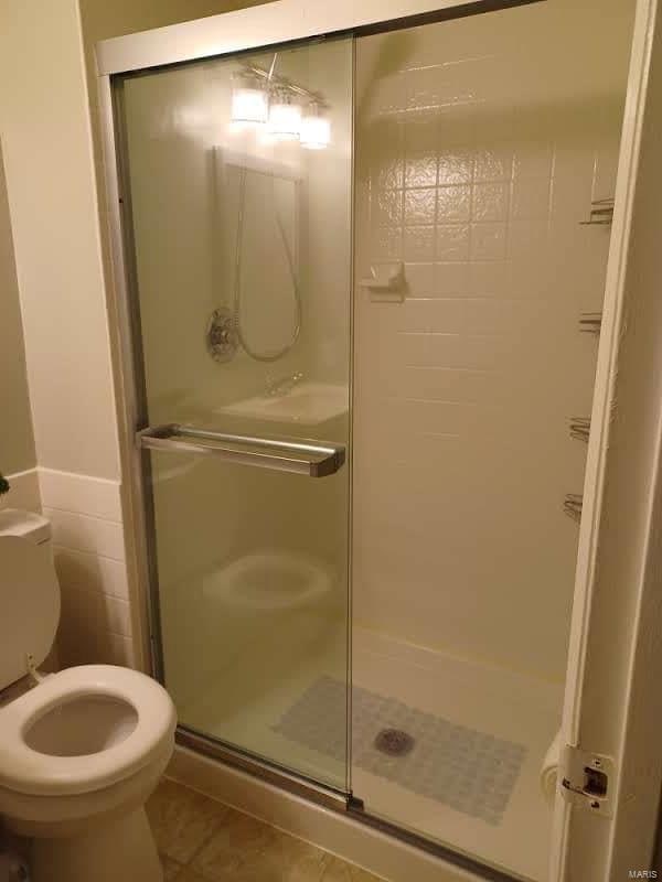 bathroom featuring an enclosed shower, tile patterned flooring, and toilet