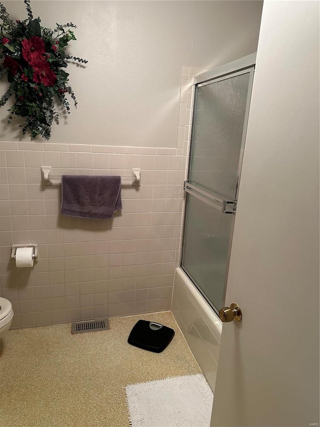 bathroom with tile walls, toilet, and combined bath / shower with glass door