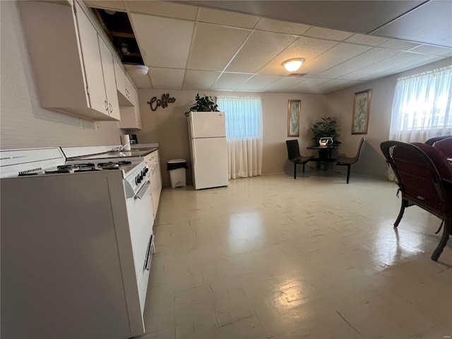 kitchen featuring white appliances, light tile patterned floors, white cabinetry, and a drop ceiling