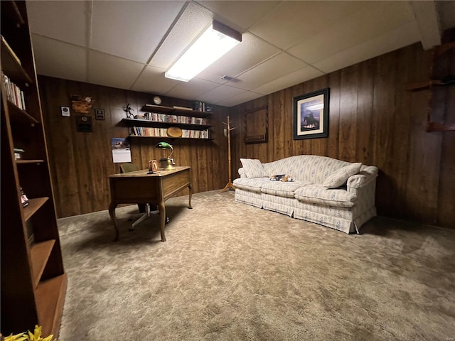 sitting room with a drop ceiling, wooden walls, and carpet flooring