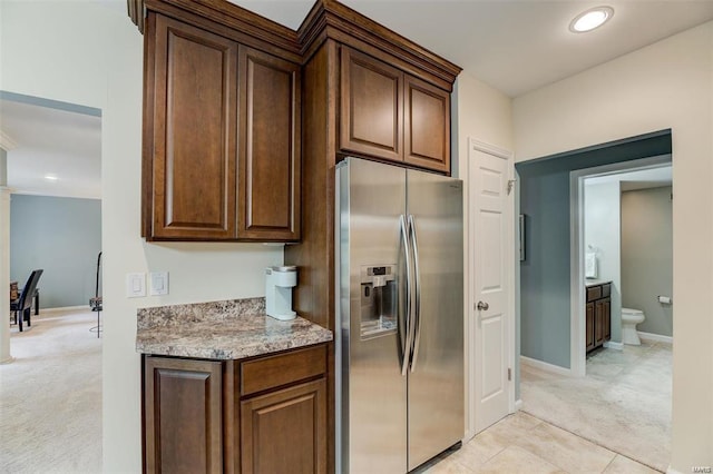 kitchen with light tile patterned flooring, stainless steel fridge, and light stone countertops