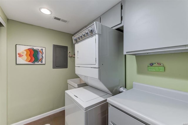 washroom with cabinets, stacked washer and clothes dryer, and electric panel