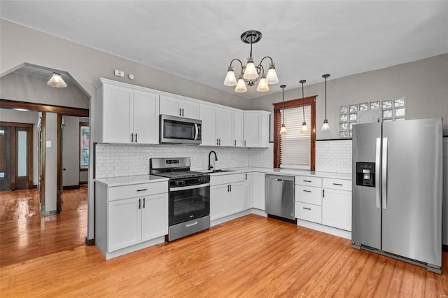 kitchen featuring hanging light fixtures, sink, appliances with stainless steel finishes, light hardwood / wood-style flooring, and backsplash