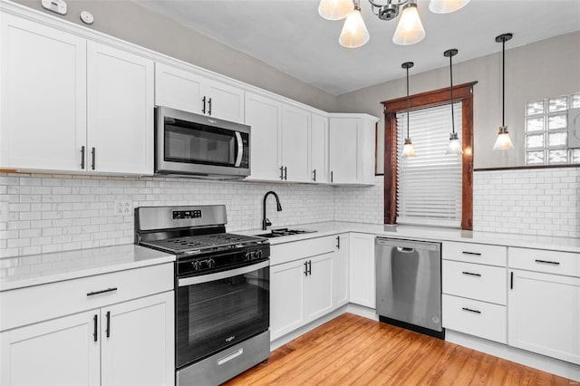 kitchen featuring stainless steel appliances, hanging light fixtures, white cabinets, light hardwood / wood-style flooring, and backsplash