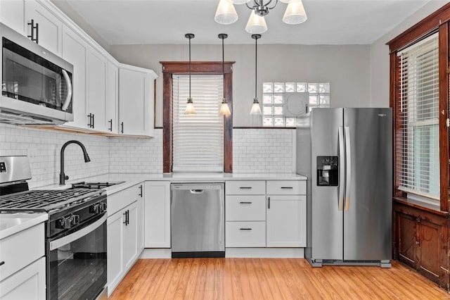 kitchen with white cabinetry, tasteful backsplash, hanging light fixtures, light hardwood / wood-style floors, and appliances with stainless steel finishes