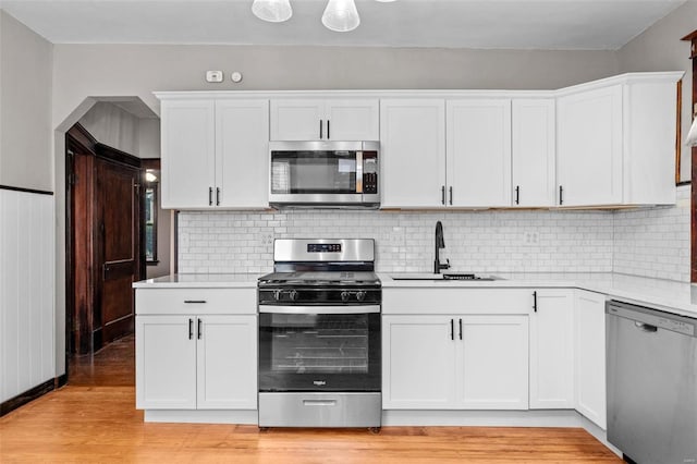 kitchen featuring stainless steel appliances, sink, backsplash, light hardwood / wood-style floors, and white cabinetry