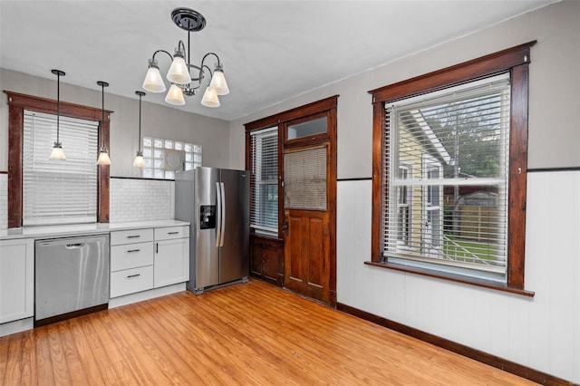 kitchen with stainless steel appliances, backsplash, light hardwood / wood-style floors, decorative light fixtures, and a notable chandelier