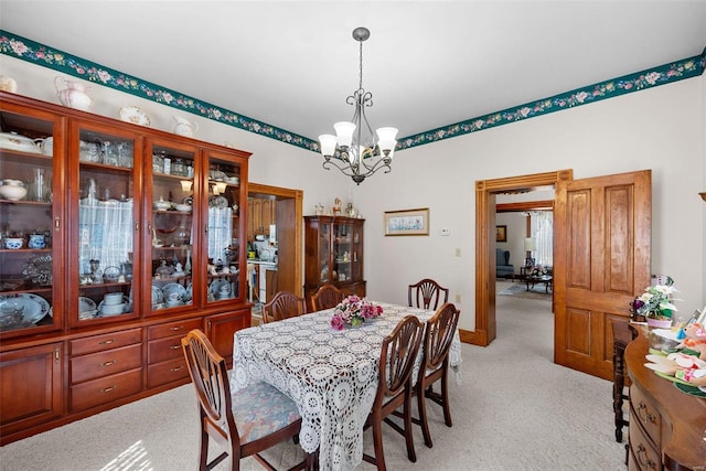 dining area featuring a chandelier, light colored carpet, and baseboards